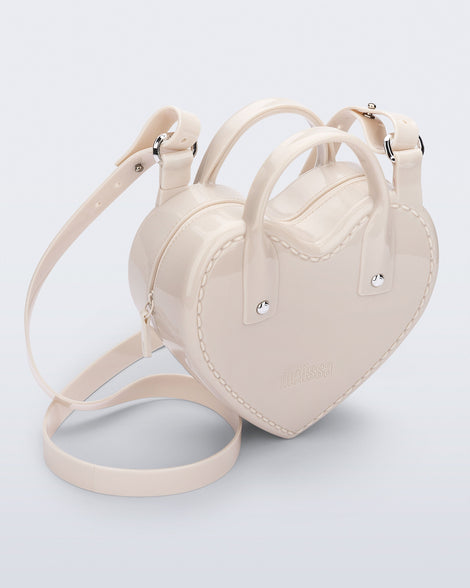 Angled view of a beige Heartbeat bag with small handles and longer strap.