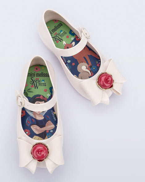 Top view of a pair of white Sweet Love Snow White baby flats with a white bow with red apple center