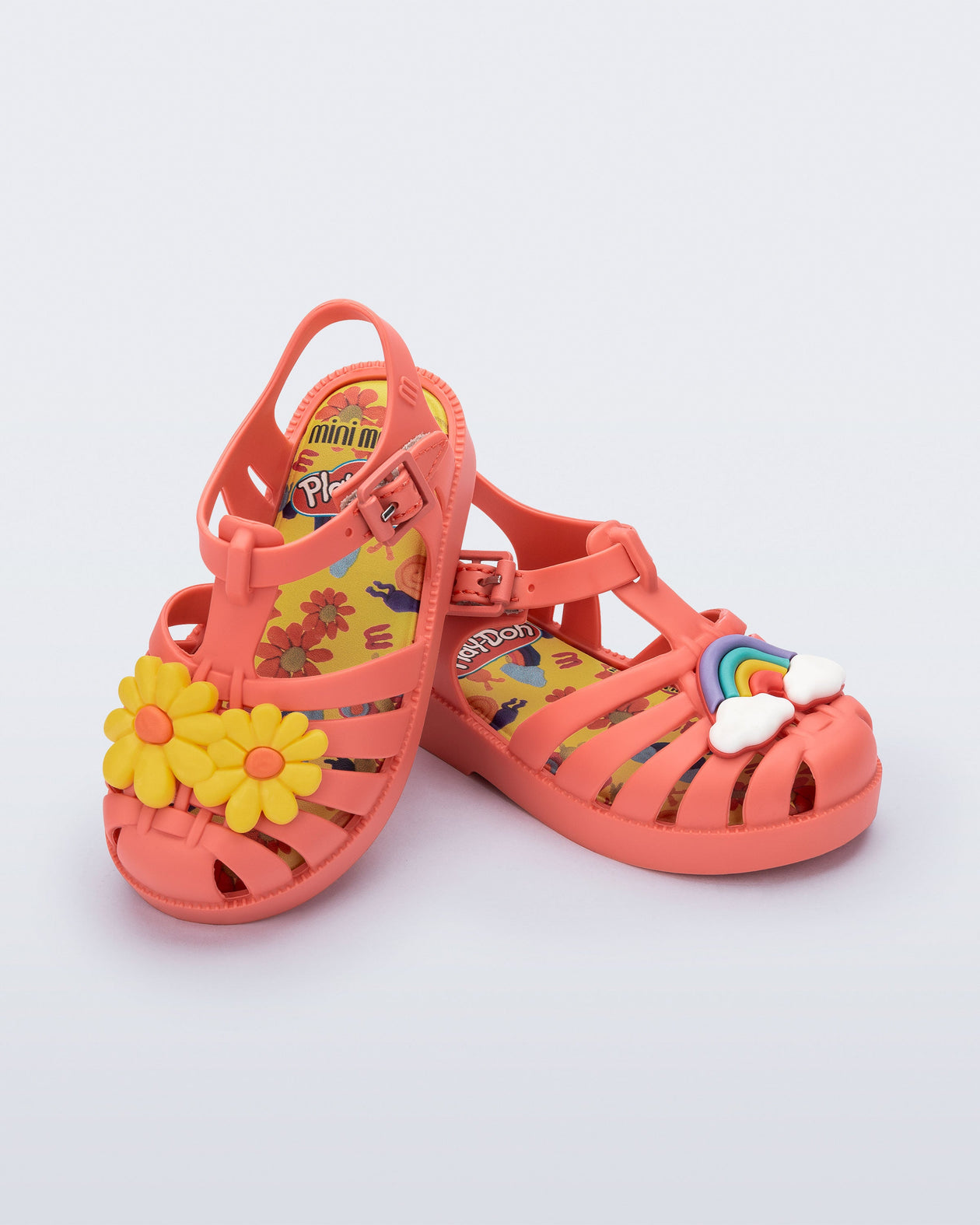 Angled view of a matte red baby Possession + Play Doh sandal with one shoe having a daisy and the other a rainbow on the upper