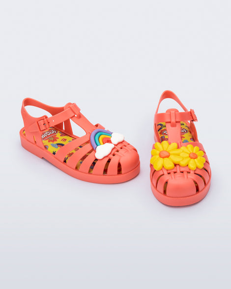 Angled view of a matte red kids Possession + Play Doh sandal with one shoe having a daisy and the other a rainbow on the upper