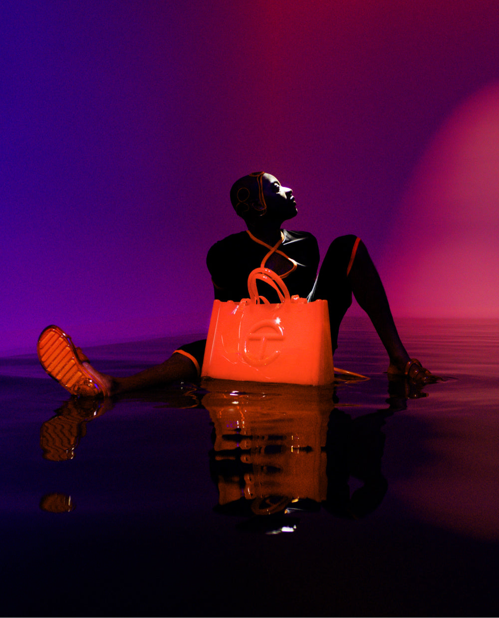 model sitting in water with the orange telfar shopper