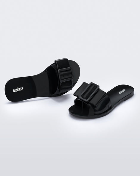 An angled front and top view of a black Melissa Babe slide with a buckle like bow detail on the front strap.