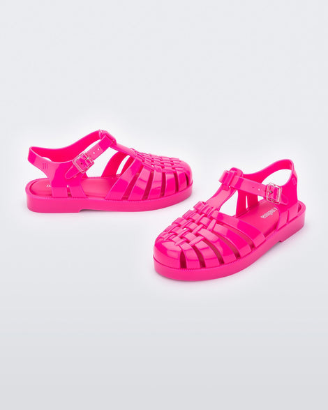 An angled front and side view of a pair of pink Mini Melissa Possession sandals with several straps, a closed toe front and a back ankle strap.