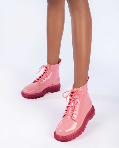 A model's legs wearing a pair of clear pink/pink Melissa Coturno boots with a pink base, laces and sole.