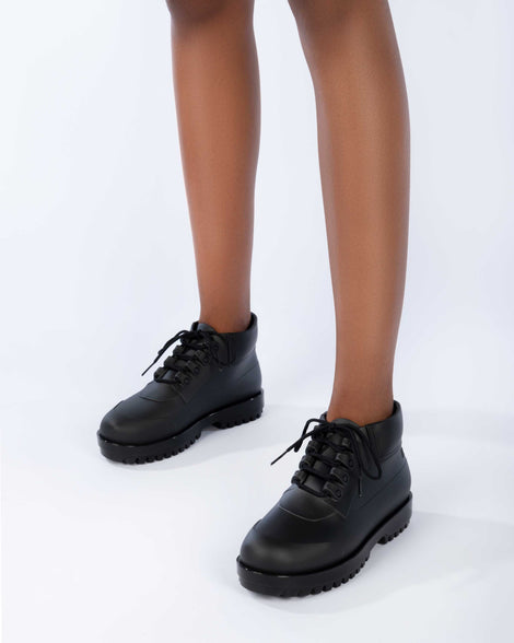 A model's legs wearing a pair of matte black Melissa Ares combat boots with a black base, laces and tractor sole.