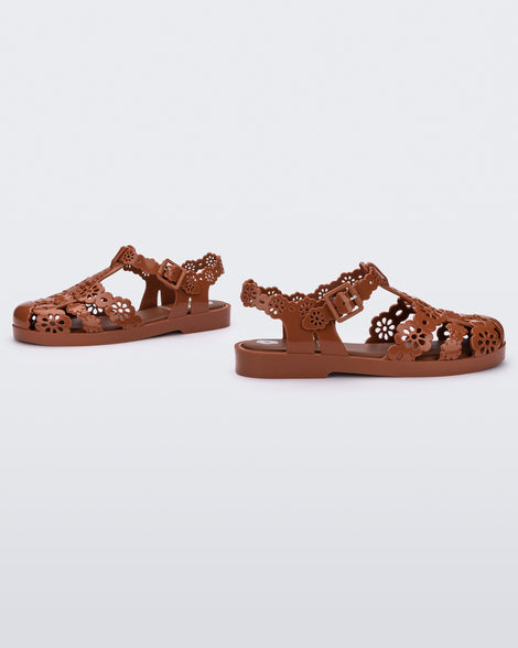 Angled view of a pair of Melissa Possession fisherman sandals in brown with cut out lace detail on the straps.