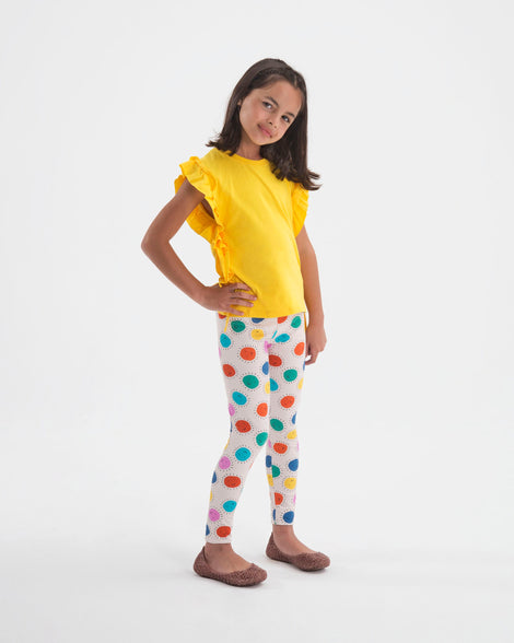 A model in a yellow shirt and polka dot leggings wearing a pair of light pink glitter Mini Melissa Campana flats with an open woven texture.