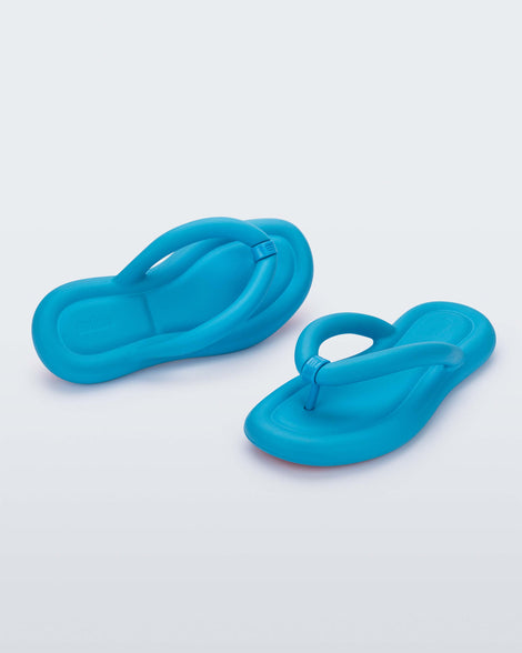 An angled back and front view of a pair of sky blue Melissa Free Flip Flops with puffer-like straps.