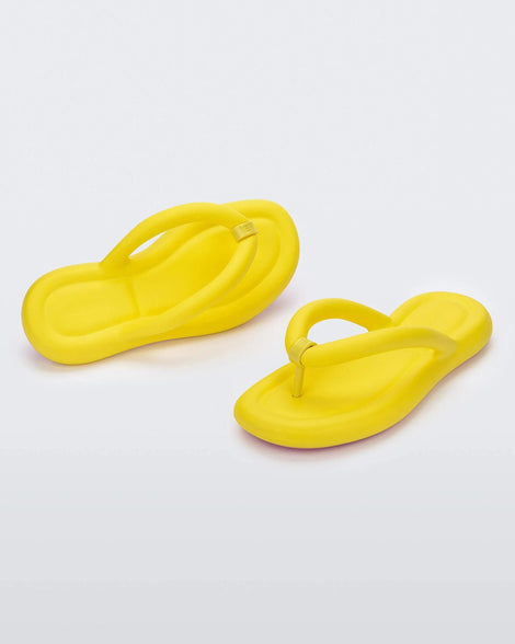 An angled front and side view of a pair of yellow Melissa Free Flip Flops with puffer-like straps.