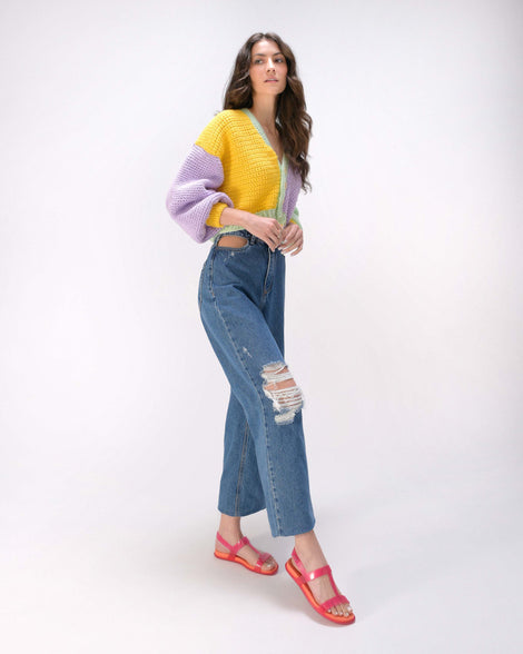 A model posing for a picture in a yellow and purple sweater, jeans and a pair of pink / orange Melissa Adore sandals with two translucent pink straps, joined together by a third strap and an orange insole.