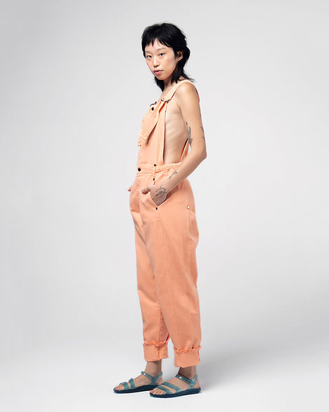 A model posing for a picture in orange overalls and wearing a pair of blue Melissa Real Jelly Sandals with two front straps and an ankle strap.