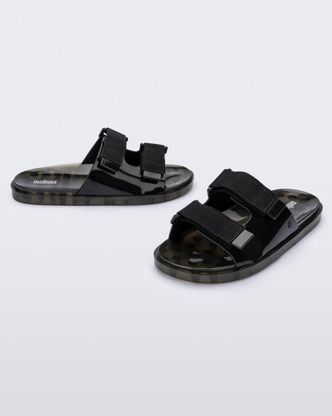 An angled front and side view of a pair of green/black Melissa Brave Wide slides with a black base, black velcro straps and a translucent green insole.