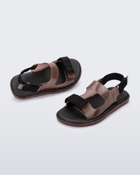 An angled front and side view of a pair of brown Melissa Brave Papete sandals with two straps, a brown base, black sole, and a front and back black velcro strap.