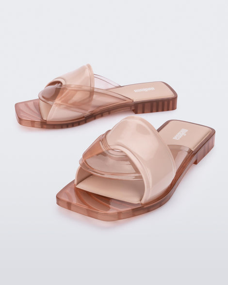 An angled front and side view of a pair of pink Melissa Brigitte slides with a solid and transparent weft designed upper strap.