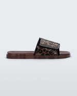 Side view of a brown / black Melissa Brave slide with a black and brown patterned velcro top strap and translucent brown insole.