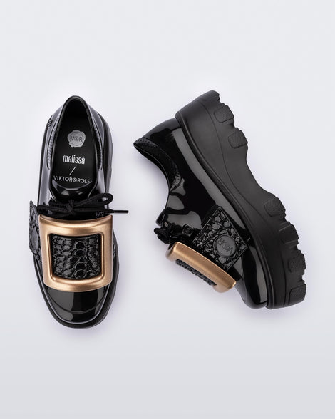 Top and side view of a pair of black Melissa Buckle Up Kick Off platform sneakers with a gold buckle.