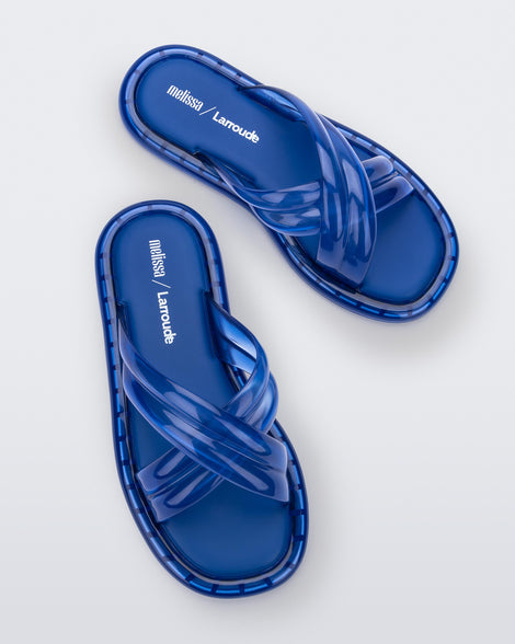 Top view of a pair of transparent blue Melissa Cali slides with cross straps.