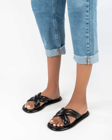 A model's legs wearing a pair of black Melissa Cali slides with cross straps.