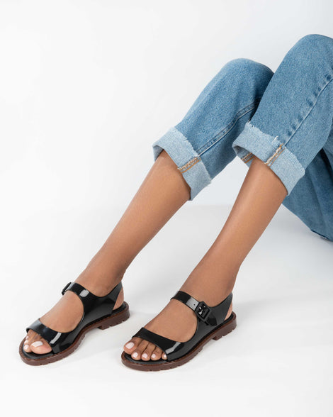 A model's legs wearing a pair of black Melissa Bae sandals with brown soles.