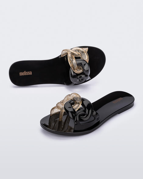 An angled top and side view of a pair of black Melissa Jelly Chain slides with a black and clear gold glitter chain detail.