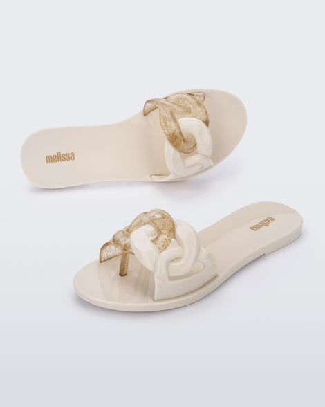 An angled top and side view of a pair of beige Melissa Jelly Chain slides with a beige and clear gold glitter chain detail.