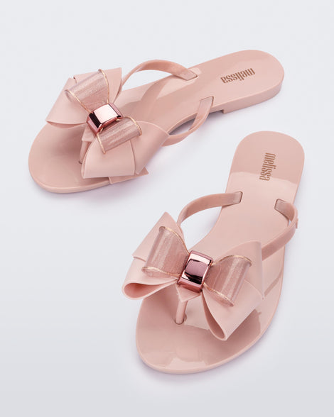 An angled top view of a pair of light pink Melissa Harmonic Sweet flip flops with a light pink and glitter bow.