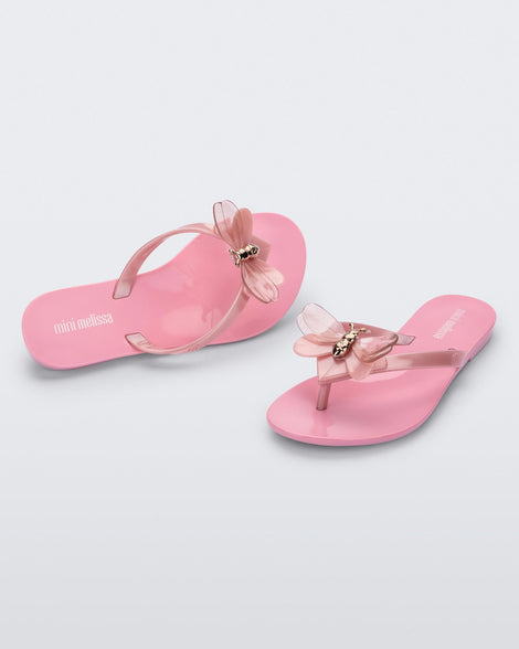 An angled front and top view of a pair of pink / pearly pink Mini Melissa Harmonic Bugs flip flops with a clear glitter bug with a gold buckle on the straps.