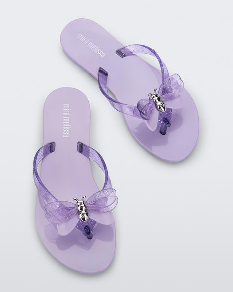 Top view of a pair of lilac / lilac glitter Mini Melissa Harmonic Bugs flip flops with a clear glitter bug with a silver buckle on the straps.