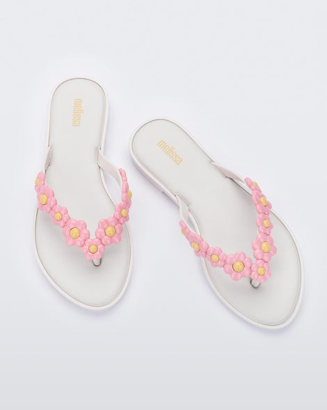 A top view of a pair of white Melissa Spring Flip Flops with pink and yellow flowers on them.