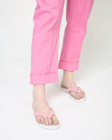 A model's legs wearing a pair of white Melissa Spring Flip Flops with pink and yellow flowers on them.