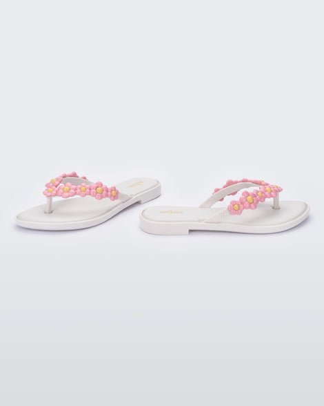 A side and front view of a pair of white Melissa Spring Flip Flops with pink and yellow flowers on them.