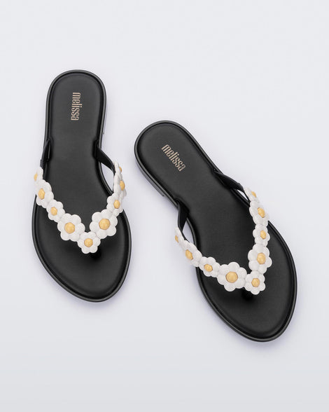 A top view of a pair of black Melissa Spring Flip Flops with white and yellow flowers on them.