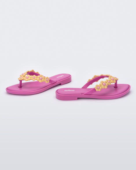 A side and angled view of a pair of pink Melissa Spring Flip Flops with yellow and pink flowers on them.