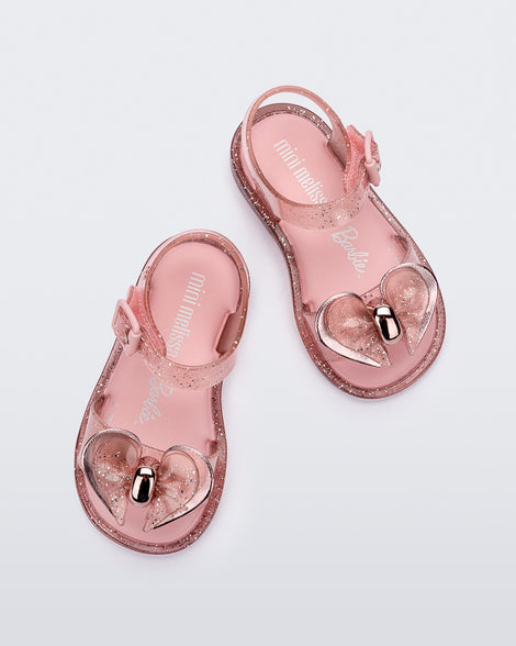 Top view of a pair of pink glitter Mini Melissa Mar sandals with a bow.