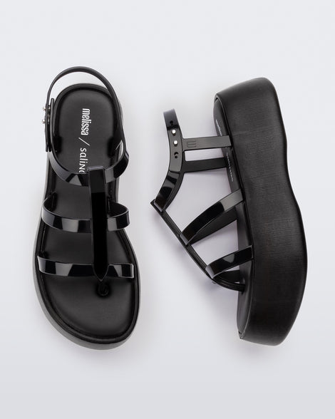 A top and side view of a pair of black Melissa Caribe High Platform sandals with two black front straps joined by a vertical strap intersecting the ankle strap and a black sole.