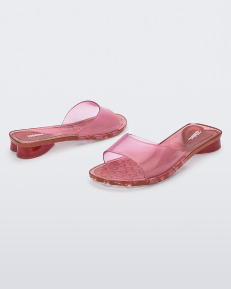 An angled front and side view of a pair of pink transparent Melissa Kim slides.