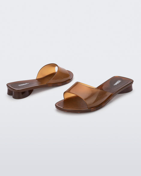 An angled front and side view of a pair of transparent brown Melissa Kim slides.