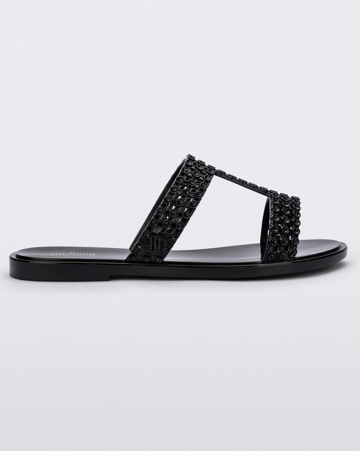 Side view of a black Melissa Glowing slide with black gem stones on the straps and a black sole.