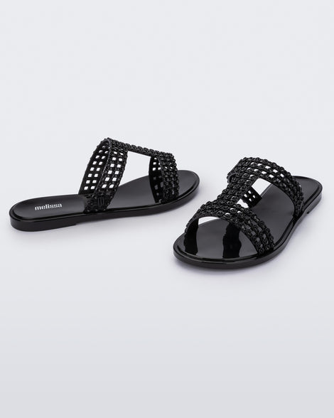 An angled side and front view of a pair of black Melissa Glowing slides with black gem stones on the straps and a black sole.