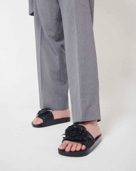 A model's legs in gray pants and a pair of black Melissa Spikes Beach slides with a flower detail and spikes on the front strap.