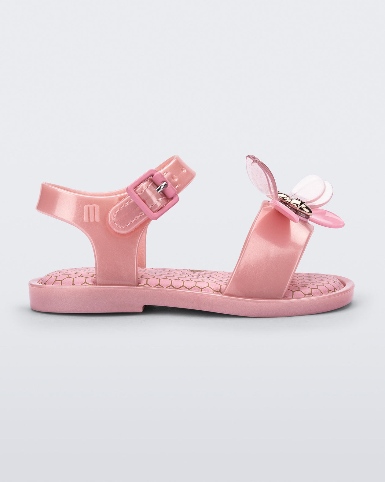 Side view of a pearly pink Mini Melissa Mar Bugs sandal with a honeycomb pattern insole and a pink bug detail with a gold buckle on the front.