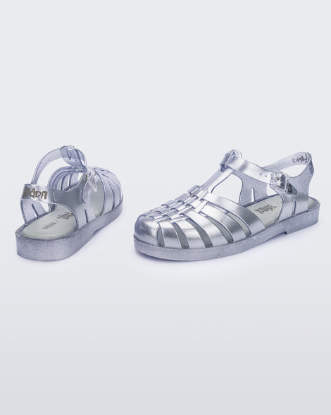 Angled view of a pair of silver Melissa Possession sandals with a closed toe front weft design connected to a top strap with a buckle.