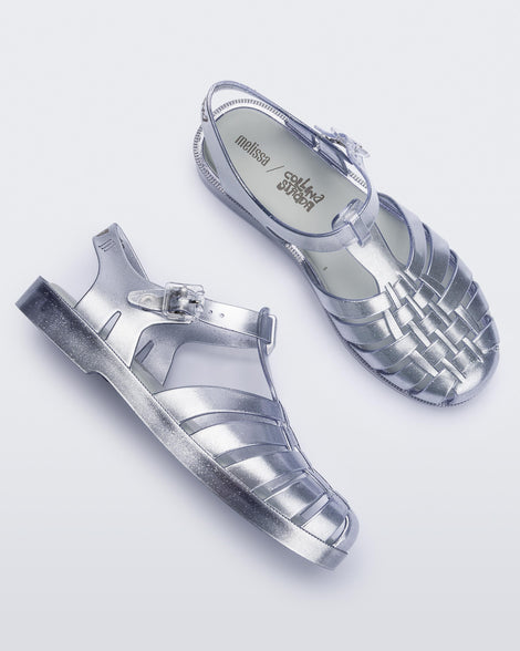 Top and side view of a pair of silver Melissa Possession sandals with a closed toe front weft design connected to a top strap with a buckle.