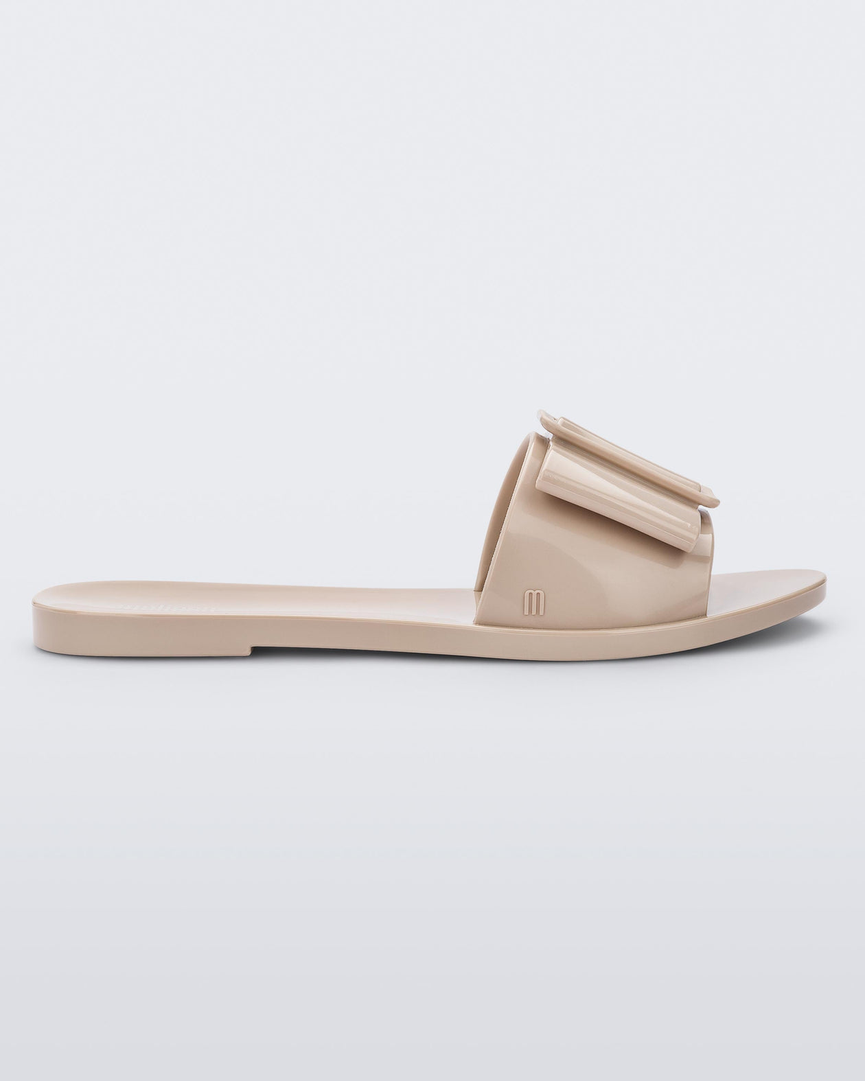 An outter side view of a Beige Melissa Babe slide with a buckle like bow detail on the front strap.