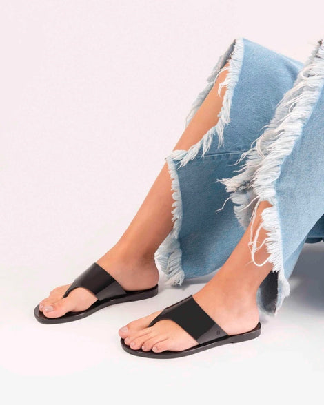 A model's legs wearing a pair of black Melissa Essential Chic Flip Flops with a wide upper strap.