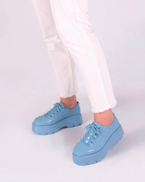 A model's legs wearing white jeans and a pair of blue platform Melissa Kick Off Sneaker with laces.