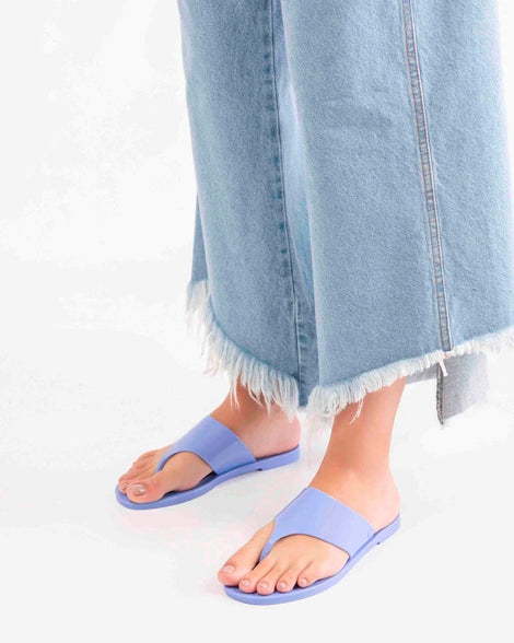 A model's legs wearing a pair of Melissa Essential Chic flip flops in Opaque Blue with thick thong straps