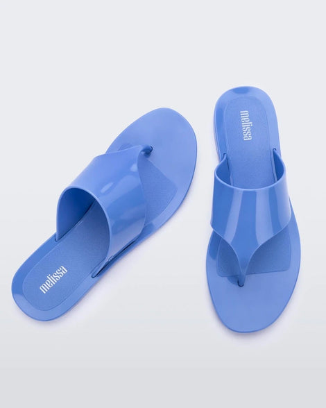 Overhead angled view of a a pair of Melissa Essential Chic flip flops in Opaque Blue with thick thong straps