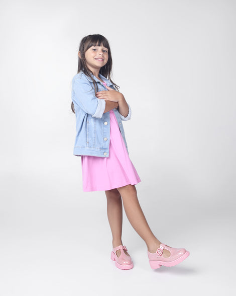 A model posing for a picture in a blue jacket, pink dress and a pair of Pink Mini Melissa Jackie loafers with a pink glitter base, two cut outs, a pink buckle detail strap and pink sole.