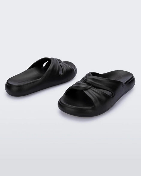 An angled side view of a pair of black Melissa Free Slides with a twist front detail.